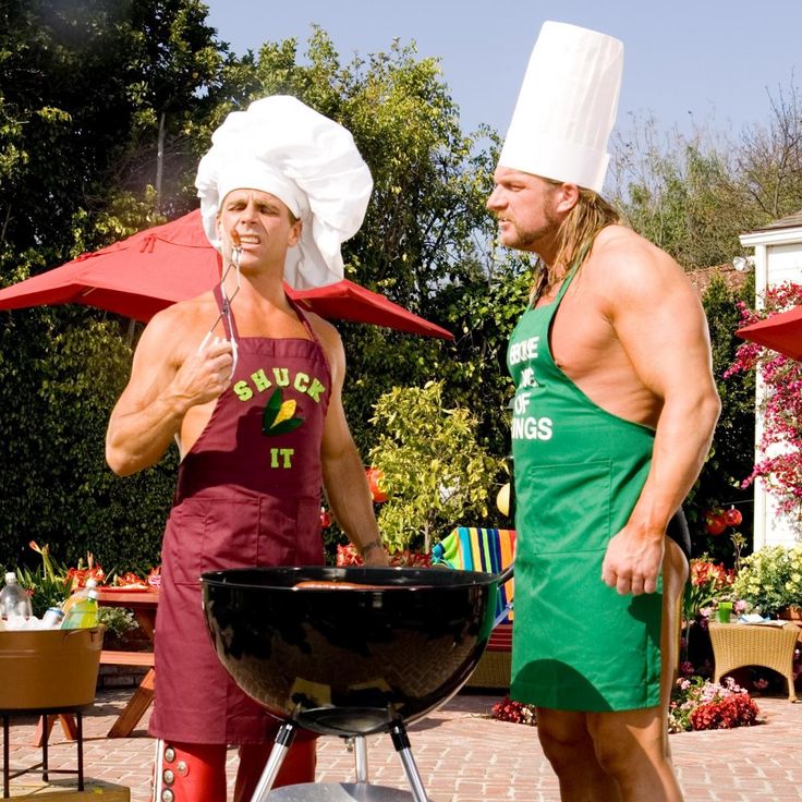 two men in aprons and hats grilling on a bbq with an umbrella