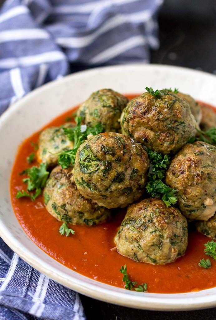 a white bowl filled with meatballs covered in sauce and garnished with parsley