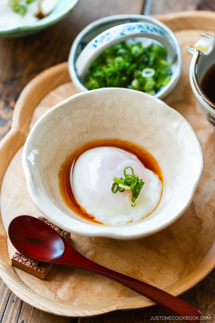 a wooden plate topped with a white bowl filled with food