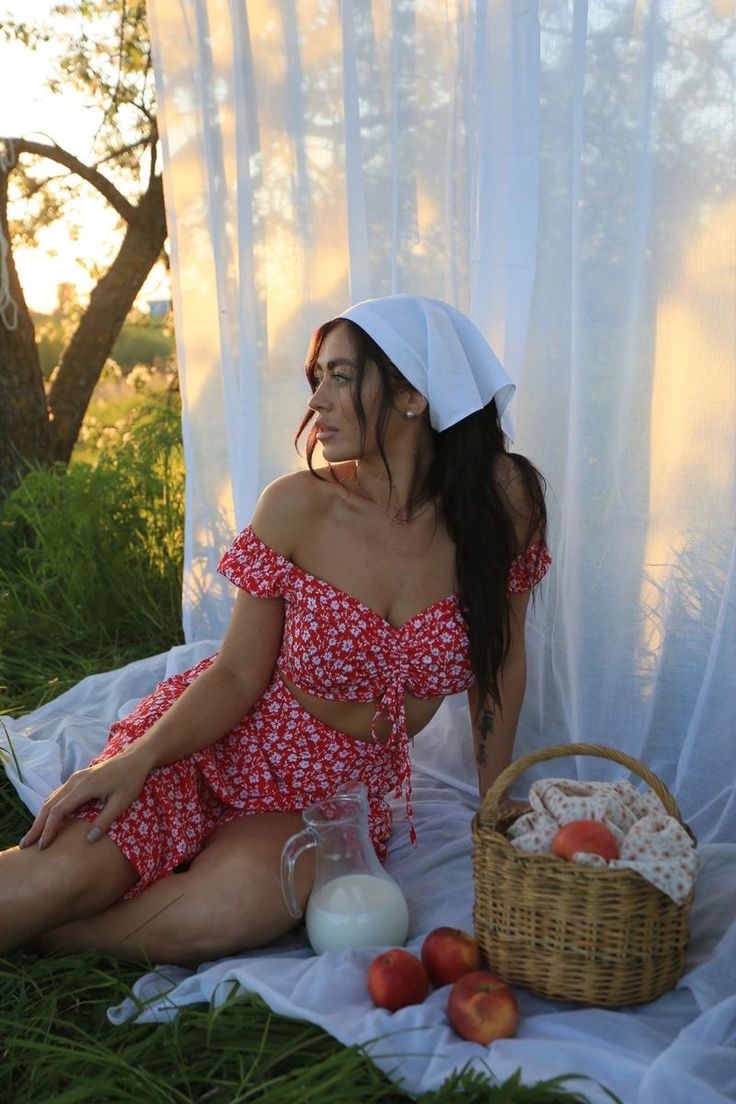 a woman is sitting on the grass with some food in front of her and an apple basket next to her