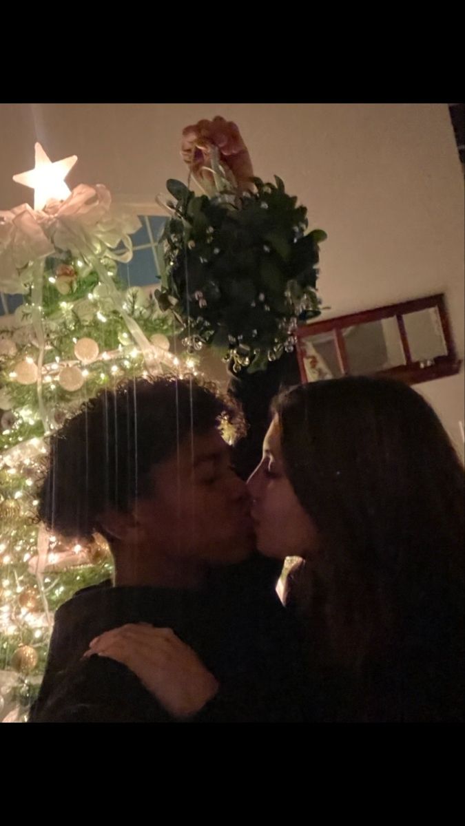 two women kissing each other in front of a christmas tree with lights and decorations on it