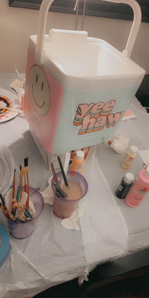 there is a cooler sitting on the table with some paint and brushes in front of it