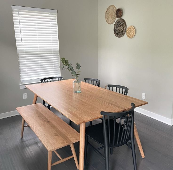 a dining room table with four chairs and a bench in front of the window,