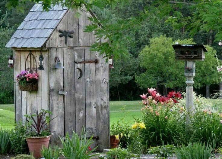 an outhouse in the middle of a garden with potted plants