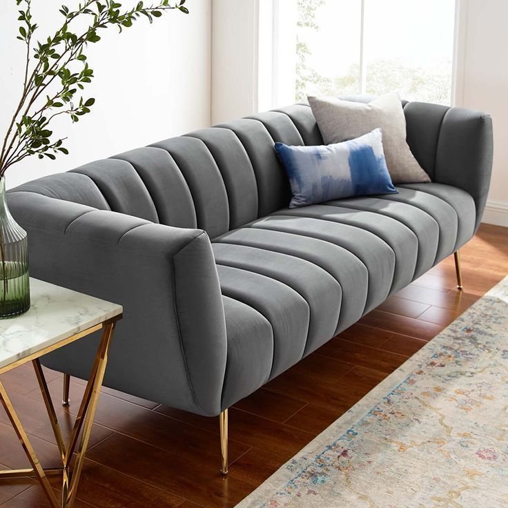 a gray couch sitting on top of a wooden floor next to a vase filled with flowers