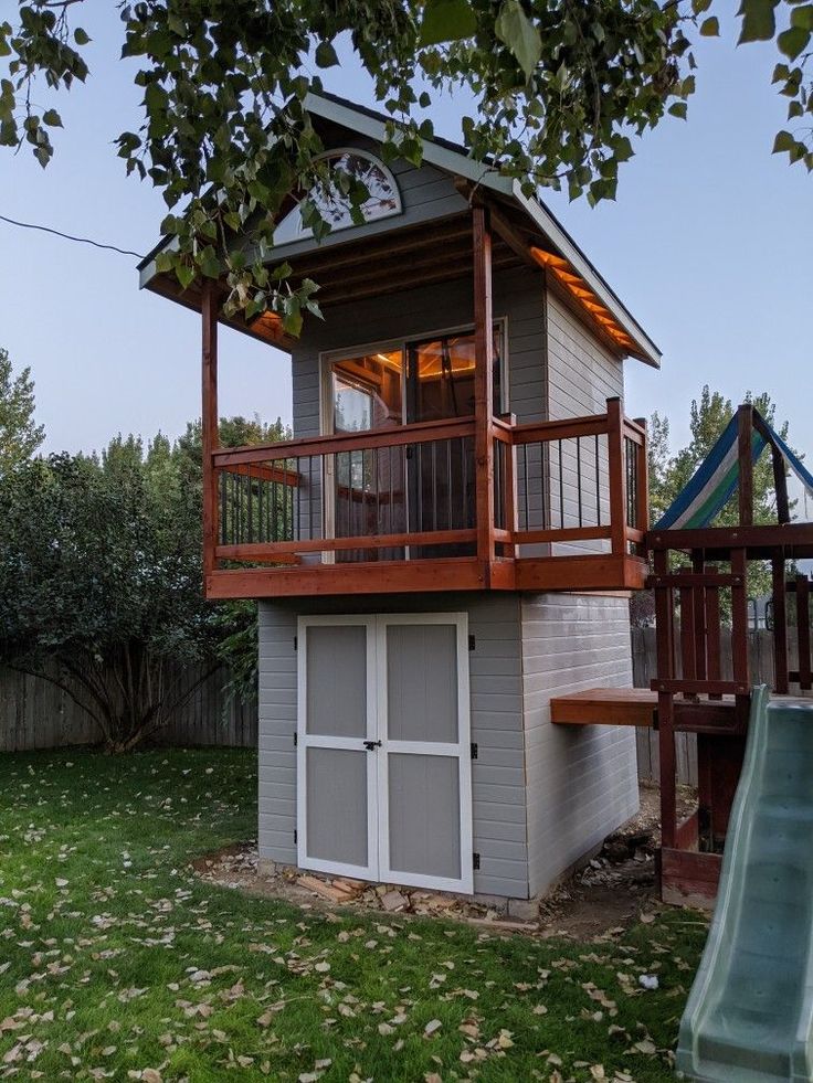 a small house with a deck and a swing set in the yard next to it