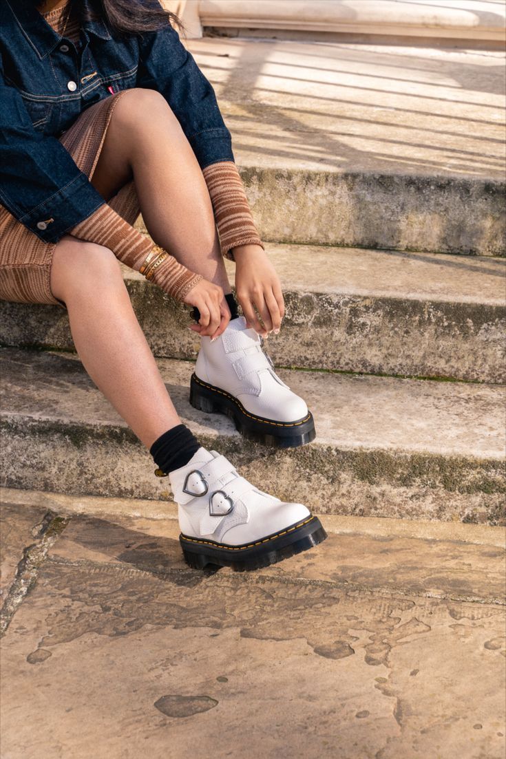 Sitting on our towering 1.5'' Quad sole and fitted with two straps woven around standout heart-shaped buckles, the Devon Heart boot offers bold, statement style. Built from fine grained Milled Nappa with padded quarters and tongue for additional comfort and finished with classic Docs DNA. Dr Martens Devon Heart, Dr Martens Devon, Womens White Boots, White Boots, Devon, Converse Sneaker, Quad, Fashion Statement, Converse