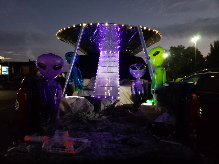 some alien statues are sitting in the back of a truck at night with lights on