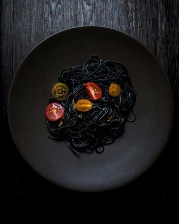 a black plate topped with pasta and tomatoes