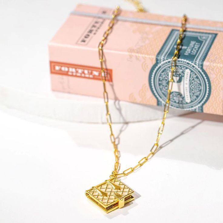 a gold necklace is sitting next to a pink bank note on a white table top