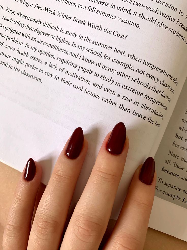 a woman's hand with dark red nail polish holding an open book