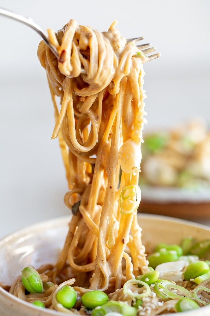 a person holding a fork full of noodles with peas and sauce on it in a bowl