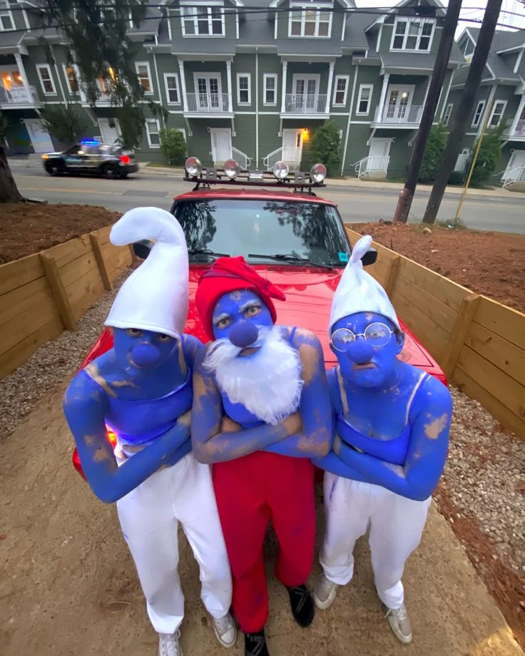 three people dressed in blue and white standing next to a red car with santa clause on it