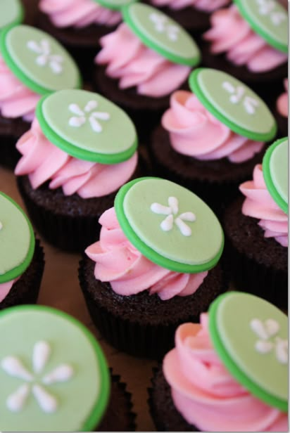 cupcakes with green and pink frosting are arranged on a table in rows