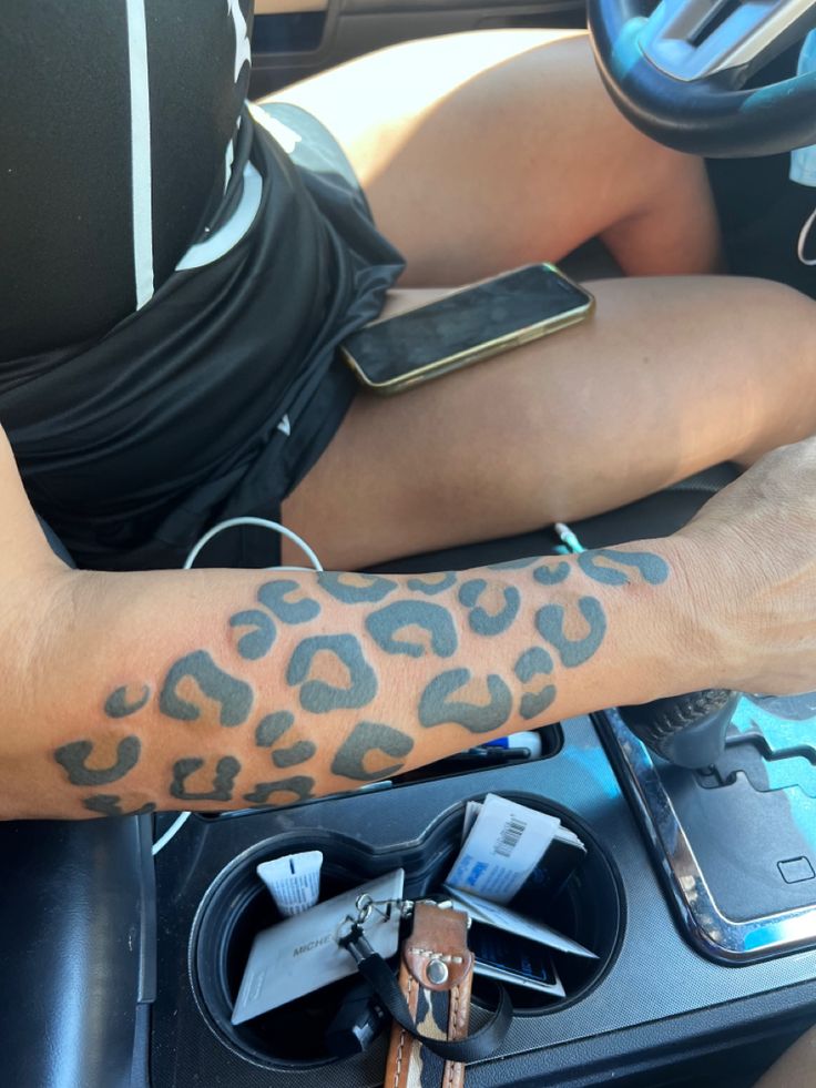 a person with a tattoo on their arm is sitting in a car and holding a cell phone