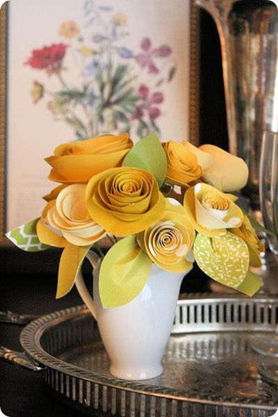 a white vase filled with yellow flowers sitting on top of a metal tray next to a mirror