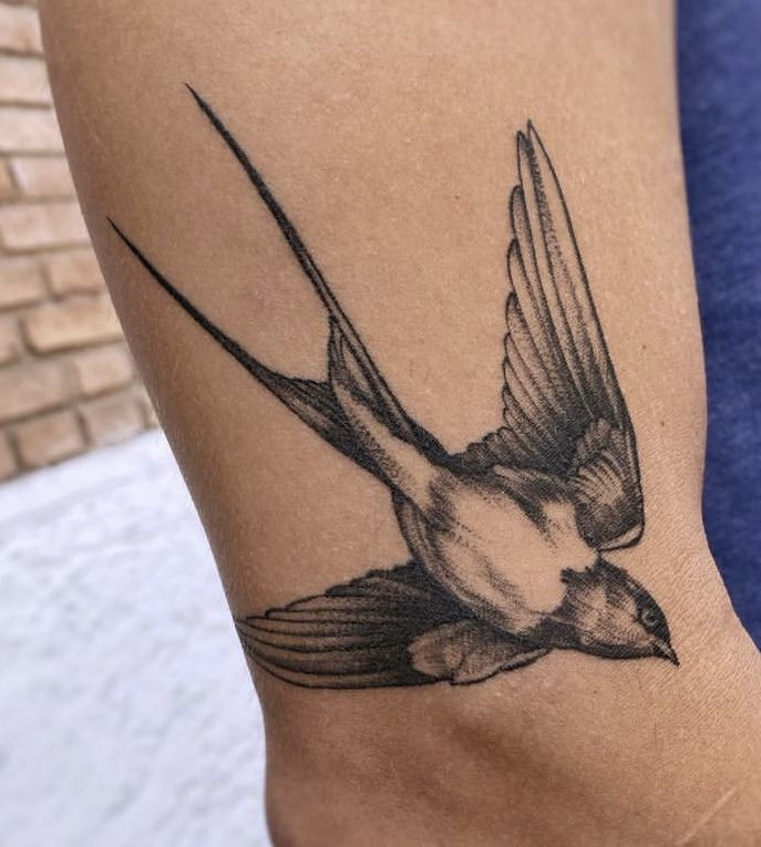 a small bird tattoo on the leg of a person's arm, with one wing extended