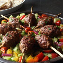 meatballs and vegetables on skewers in a bowl with pita chips next to it