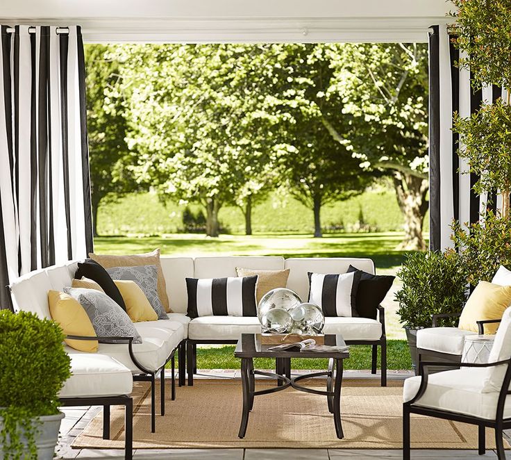 an outdoor living room with black and white striped curtains on the window sill, couches, coffee table and potted plants