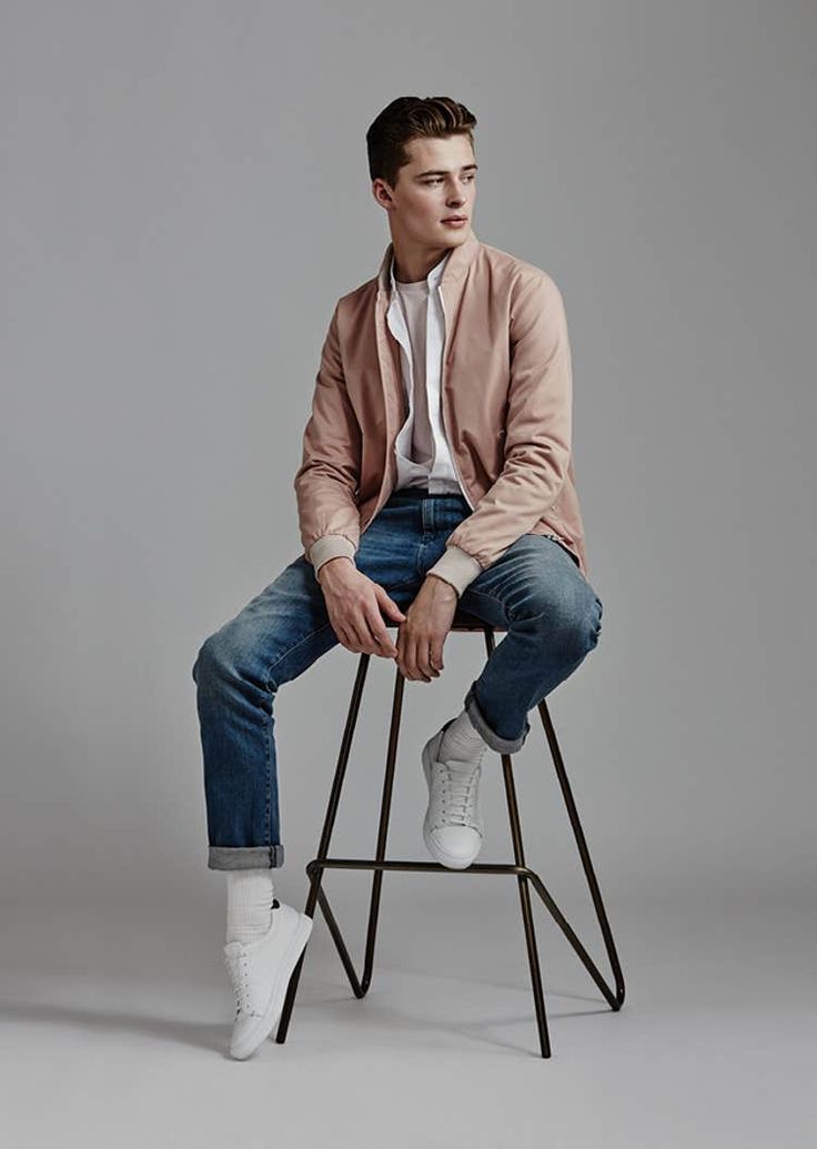 a young man sitting on top of a stool wearing jeans and a pink blazer