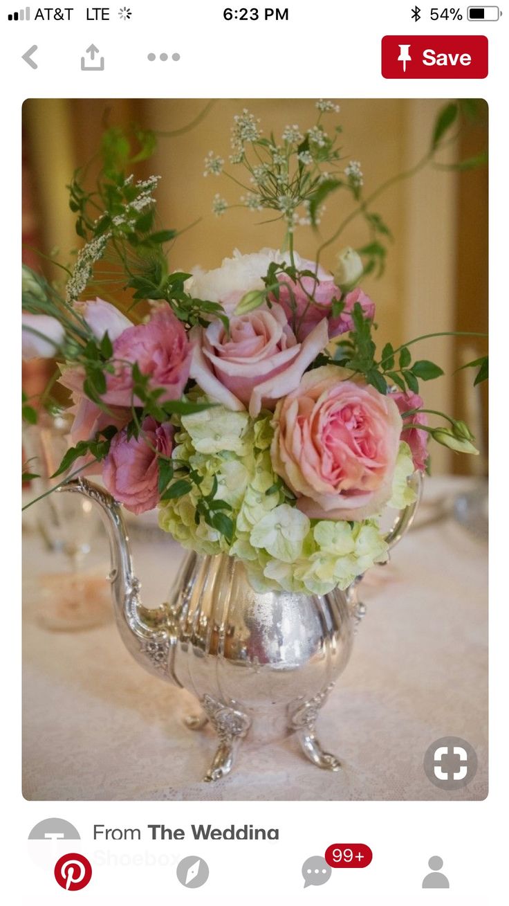 a silver tea pot with pink and white flowers in it sitting on a table cloth