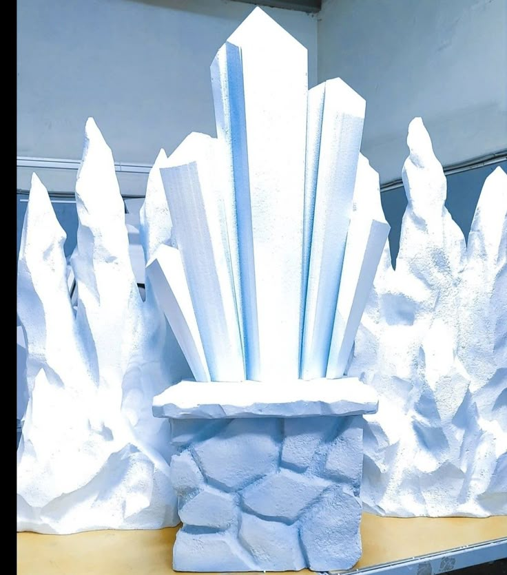 an iceberg sculpture sitting on top of a table next to snow covered rocks and trees