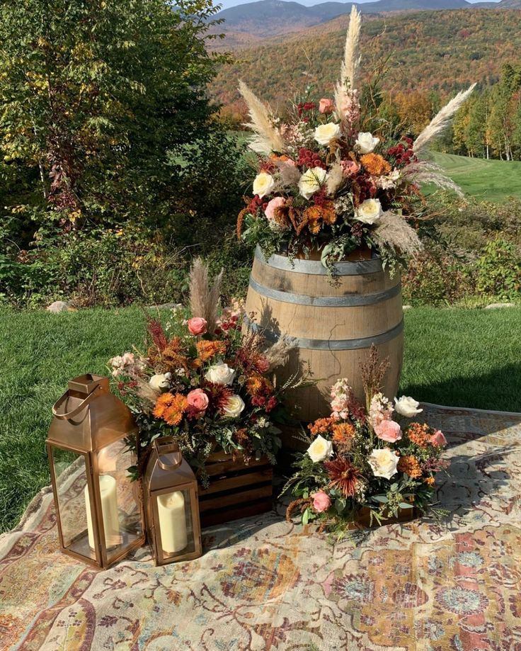 an arrangement of flowers and foliage in a barrel on a table with a mountain view