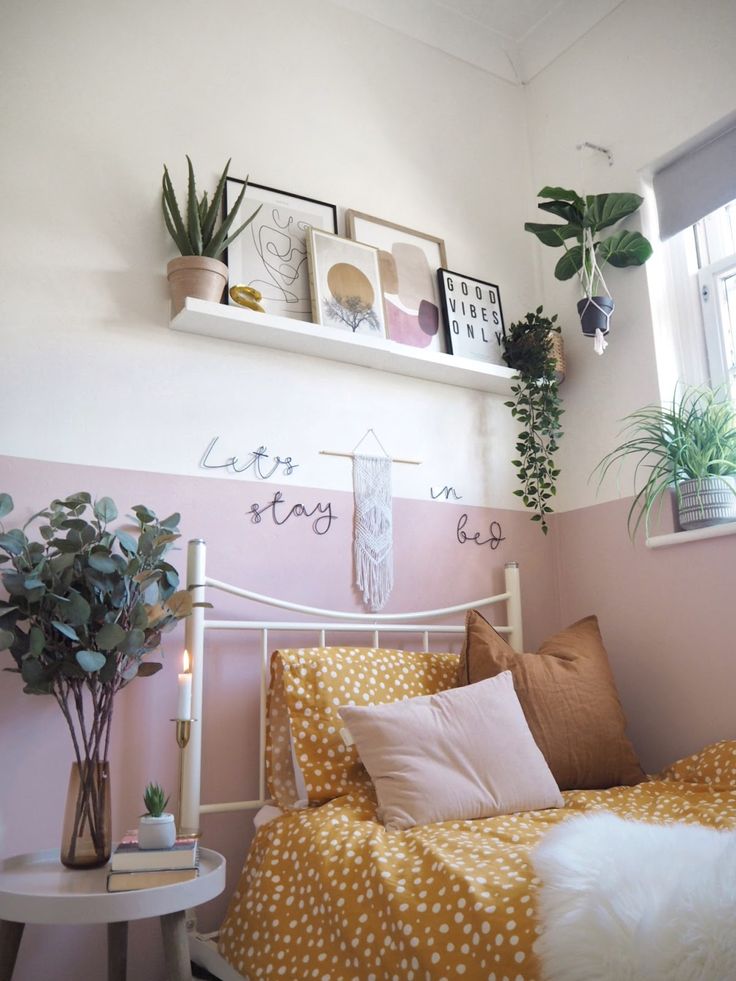 a bedroom with pink and white walls, potted plants on the shelf above the bed