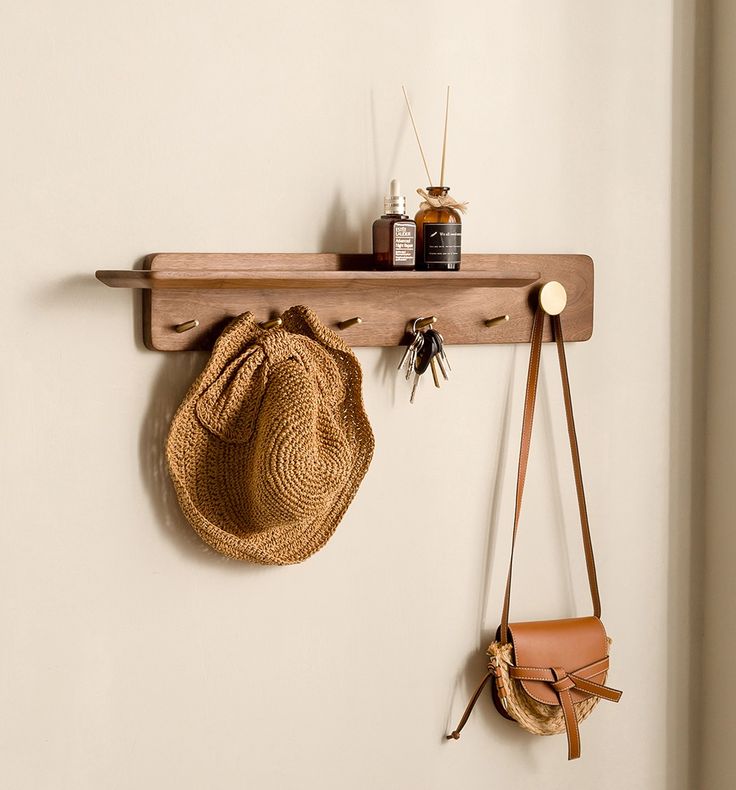 a hat and purse hanging on a wooden shelf next to a wall mounted hook with hooks