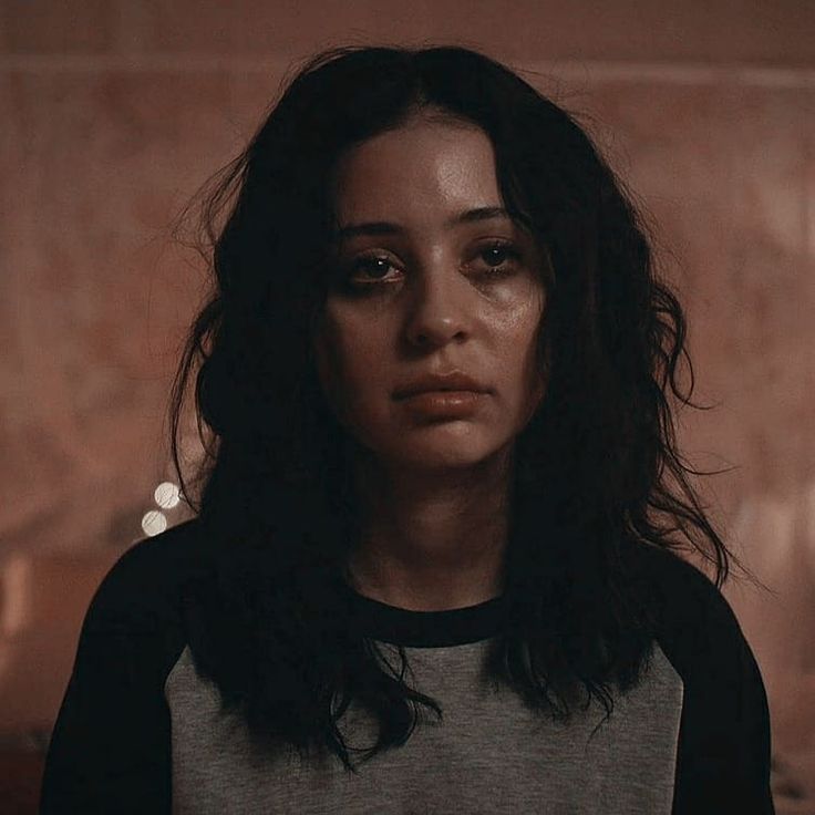 a woman with dark hair stares at the camera while standing in a dimly lit room