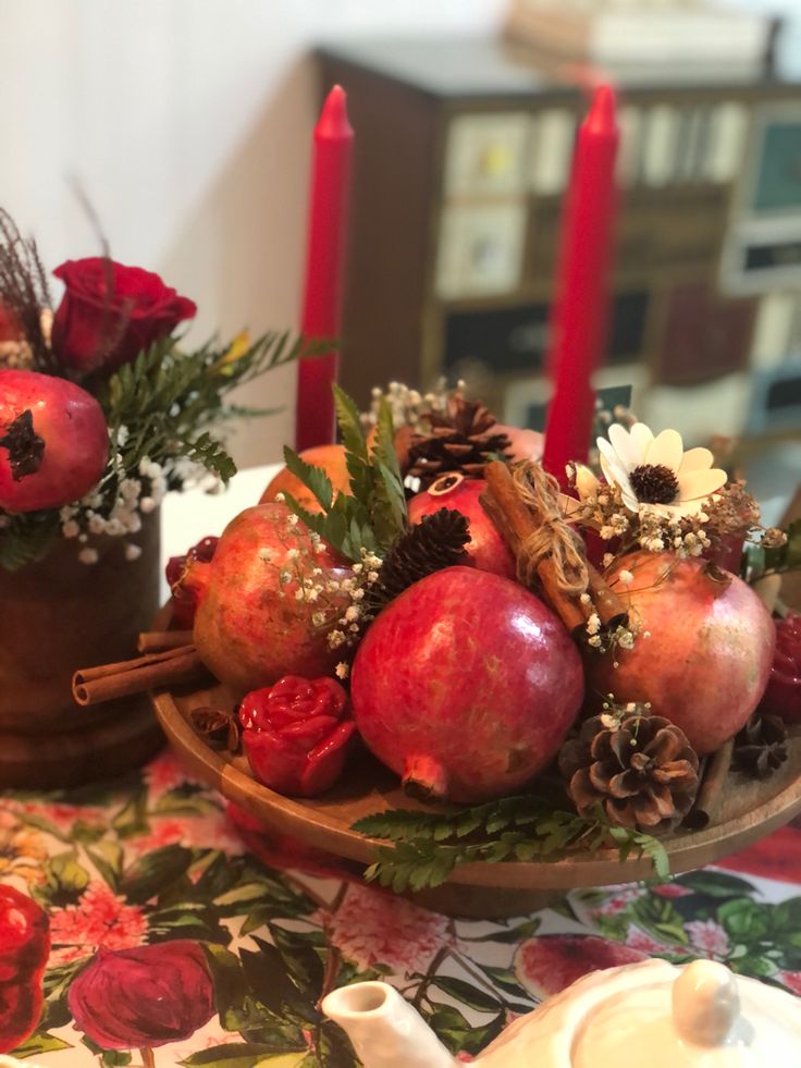 a table topped with apples and flowers on top of a wooden plate next to candles