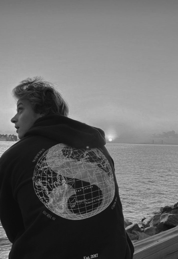 black and white photograph of a person standing near the water with a hoodie on