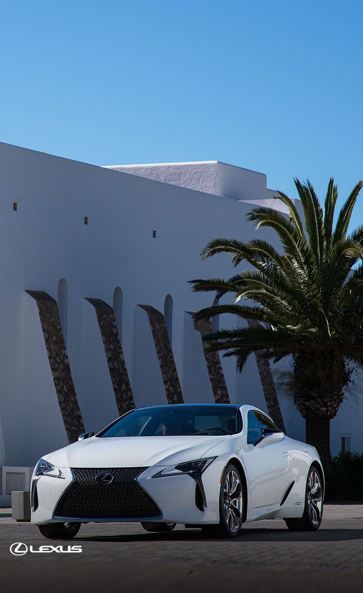 a white sports car parked in front of a building with palm trees on the side