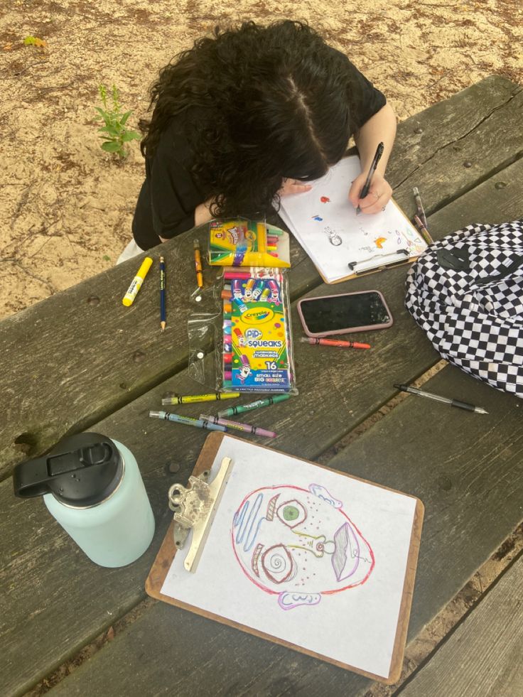 a person sitting at a picnic table with their head down and writing on a piece of paper