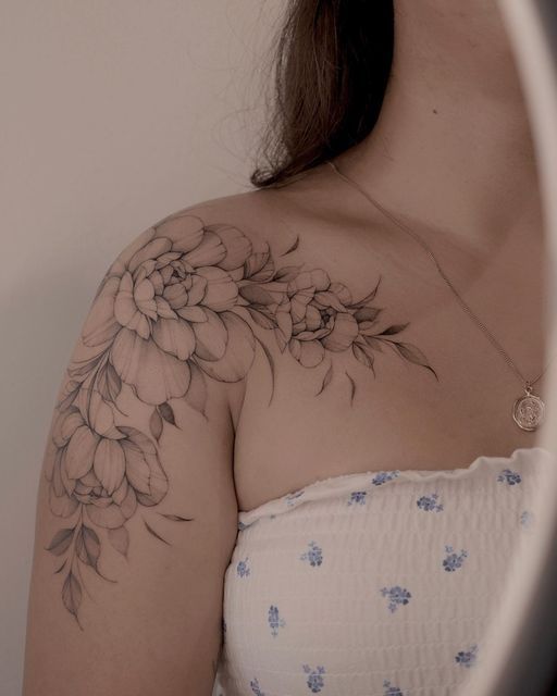 a woman with a flower tattoo on her arm and shoulder, looking at herself in the mirror