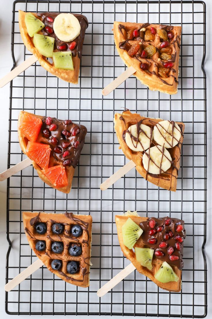 four waffles with fruit and nuts on them sitting on a wire cooling rack