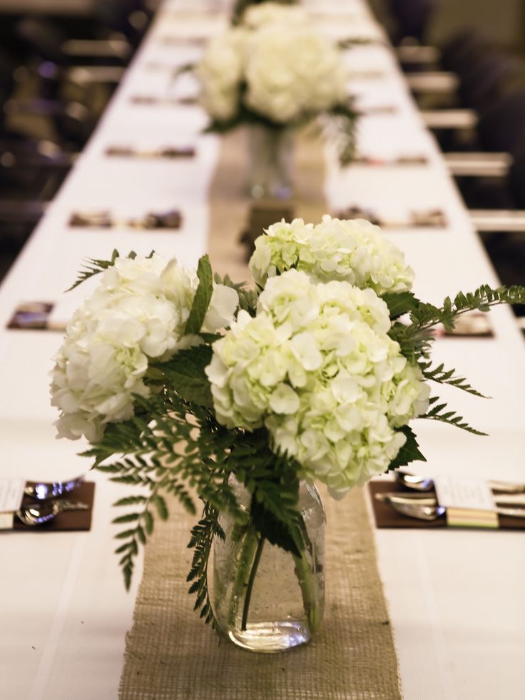 the table is set with white flowers in vases and place cards on each side