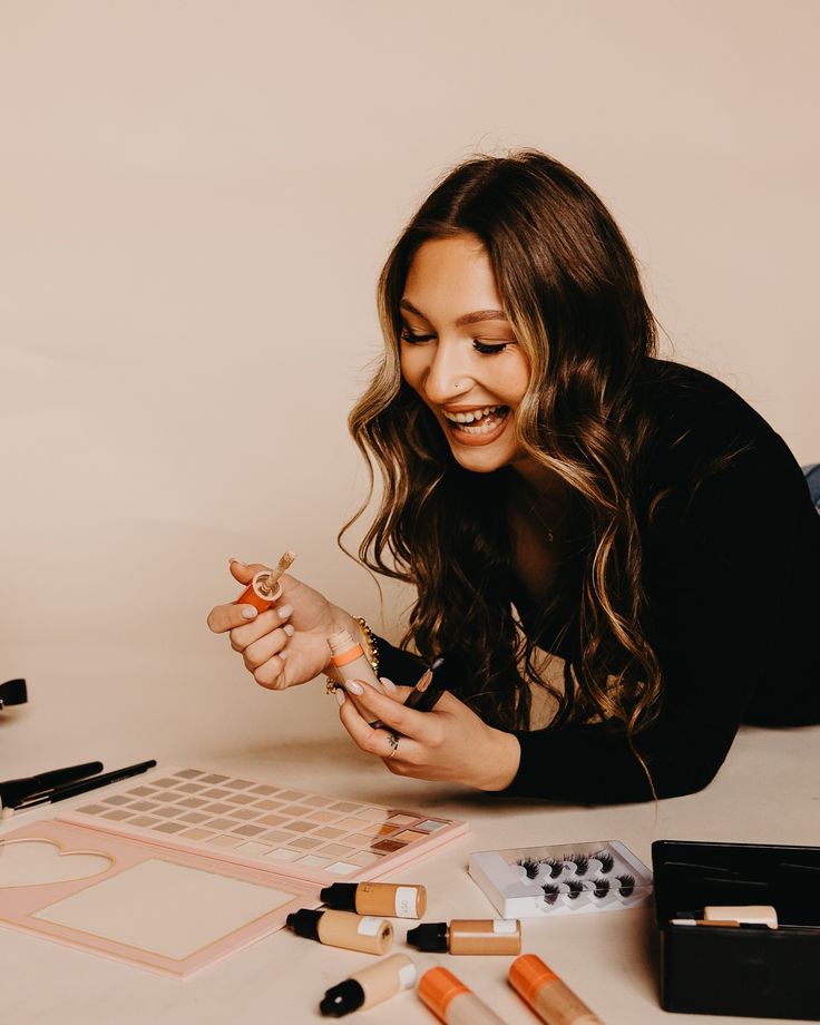 a woman laying on the floor with some makeup and brushes in her hand while looking at it