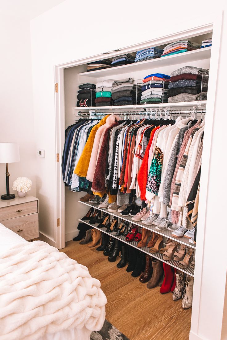 an open closet with clothes and shoes hanging on the wall, next to a bed