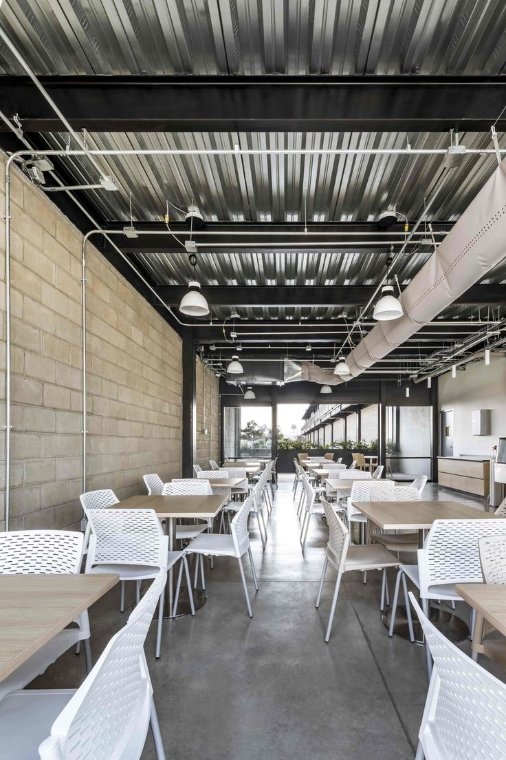 tables and chairs are lined up in an empty room with exposed metal roofing on the walls