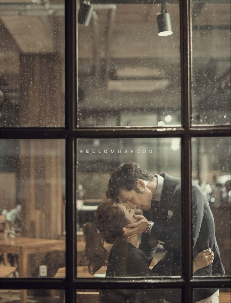 a man and woman kissing in front of a window with rain falling down on them