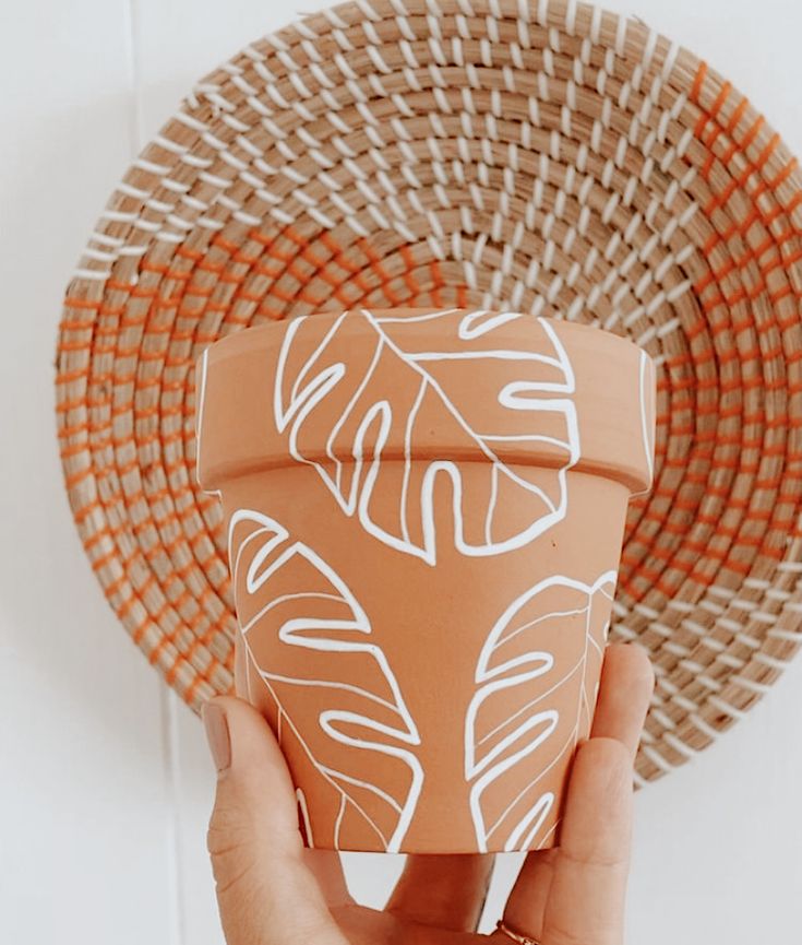 a hand is holding a clay pot with white designs on it next to a wicker plate