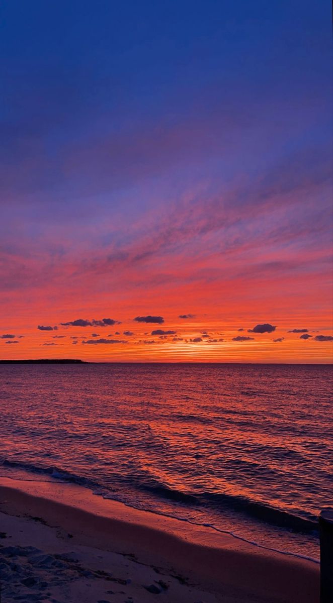 the sun is setting over the ocean and it's colors are red, orange, blue, and purple