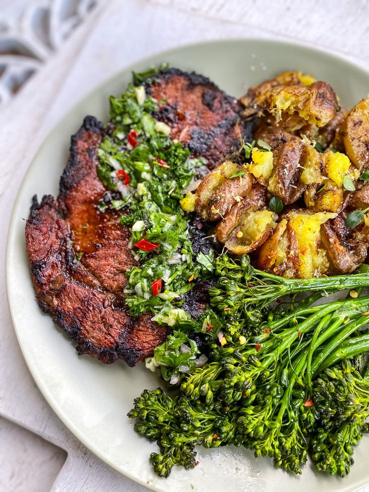 a white plate topped with meat and veggies next to broccoli on a table