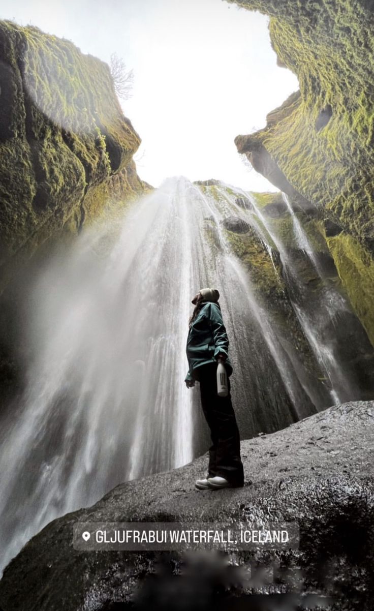 a person standing in front of a waterfall with water coming out of the ground and into the air