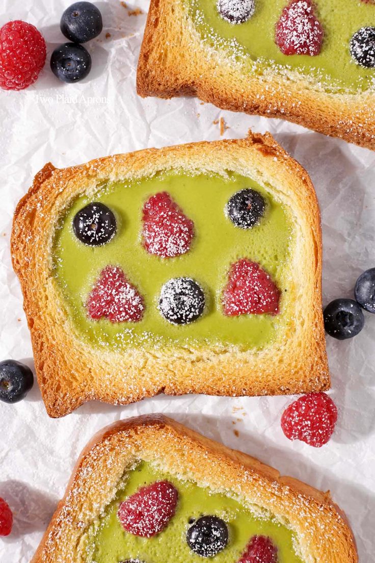 two pieces of bread with berries on top and powdered sugar on the side, sitting next to each other