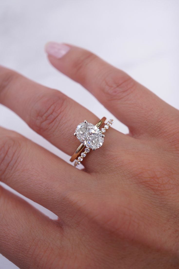 a woman's hand with a diamond ring on top of her finger and an engagement band