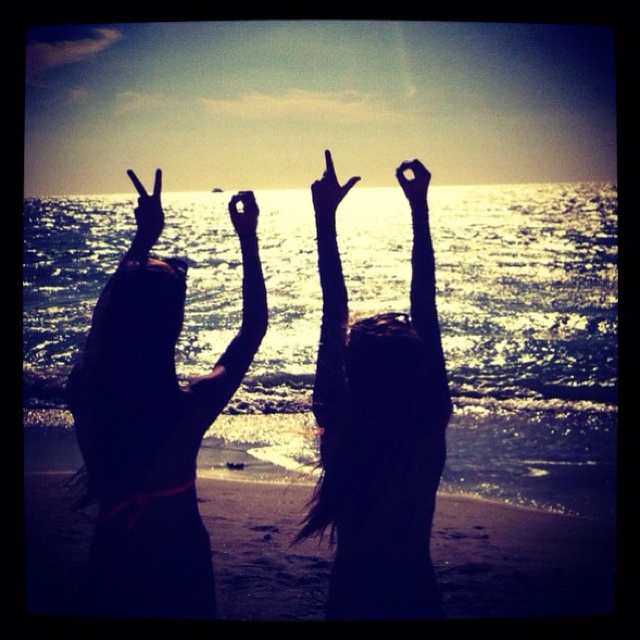 two girls standing on the beach with their arms in the air