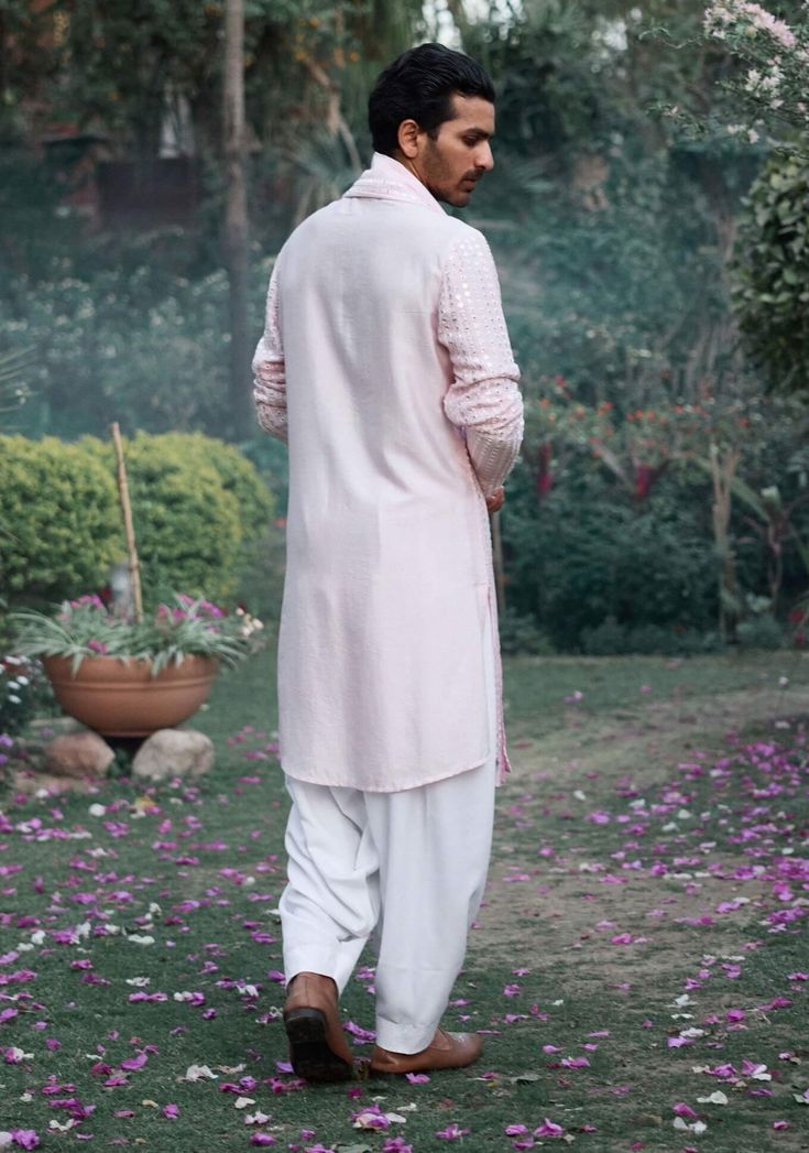 The jalalgarh kurta in powder pink is a charming and sophisticated choice for Indian grooms, ideal for haldi, mehndi, or sangeet ceremonies. Crafted from a luxurious blend of viscose cotton silk and georgette, this kurta offers a smooth and breathable feel, perfect for long celebrations. The kurta comes with an ivory salwar, creating a balanced and harmonious ensemble. The jalalgarh kurta is perfect for grooms who want a contemporary yet traditional outfit. Pair it with traditional juttis or modern footwear for a polished and sophisticated appearance. Pink Bandhgala With Dabka Work For Eid, Pink Bandhgala With Dabka Work, Pink Long Sleeve Sherwani With Dabka Work, Pink Straight Kurta With Cutdana, Pink Cotton Sherwani With Resham Embroidery, Pink Bandhgala With Chikankari Embroidery, Festive Pink Bandhgala With Naqshi, Pink Straight Kurta Bandhgala For Festivals, Pink Kurta With Chikankari Embroidery For Transitional Season