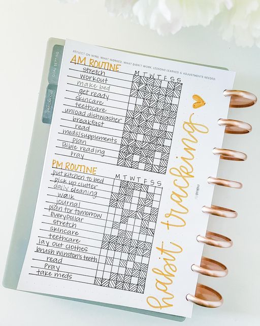 an open planner with gold foil lettering on it and some flowers in the back ground